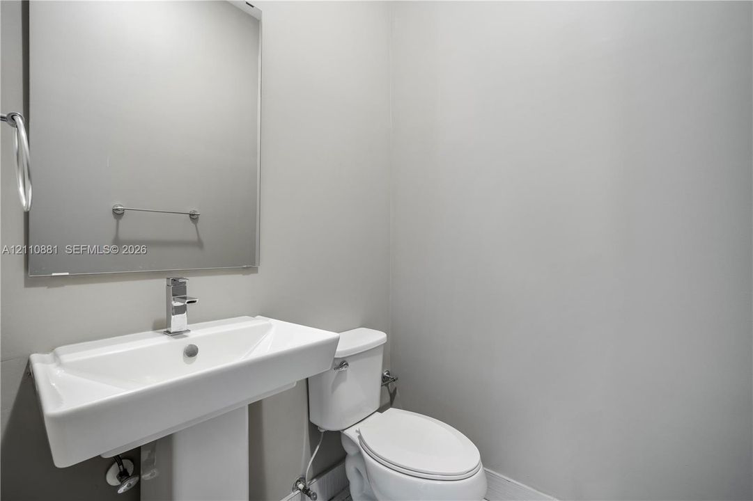 Wall-mounted rectangular mirror, pedestal sink with a chrome single-handle faucet, and a dual-flush toilet