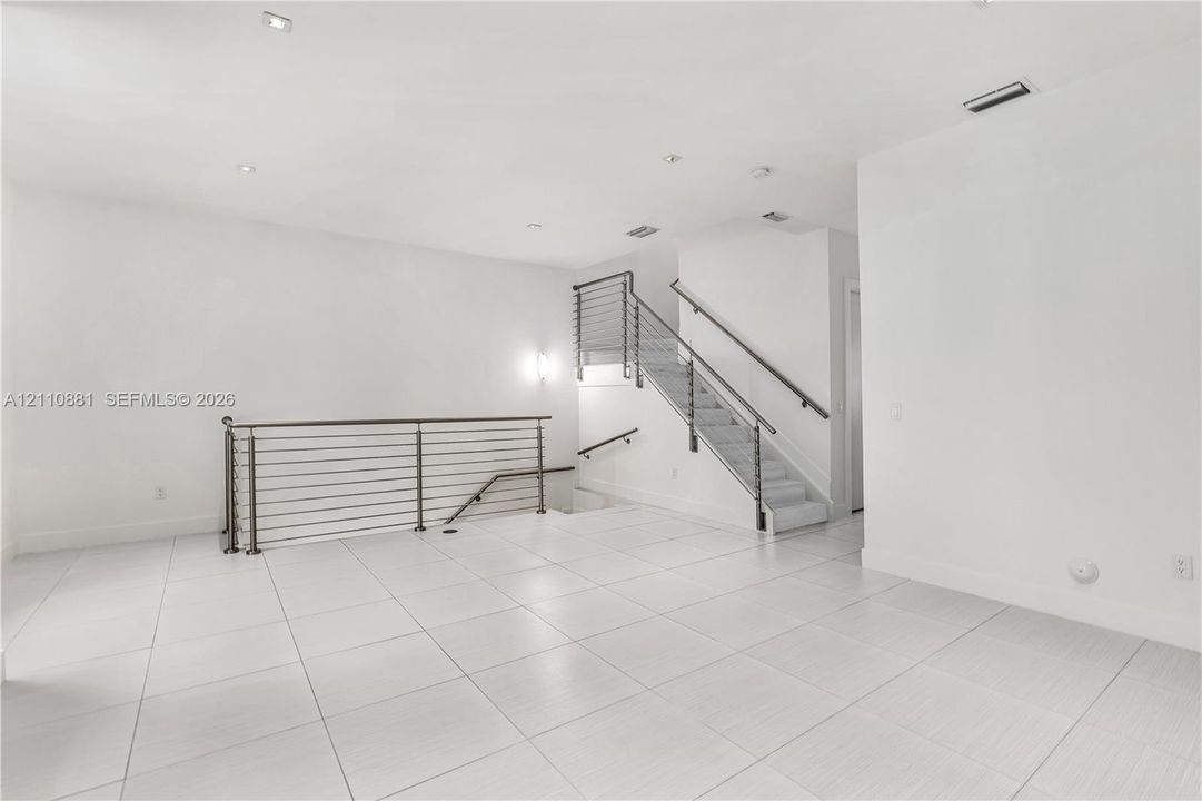Open interior featuring large-format ceramic tile flooring, recessed ceiling lighting, and a staircase with metal horizontal railing and wood-finish handrail