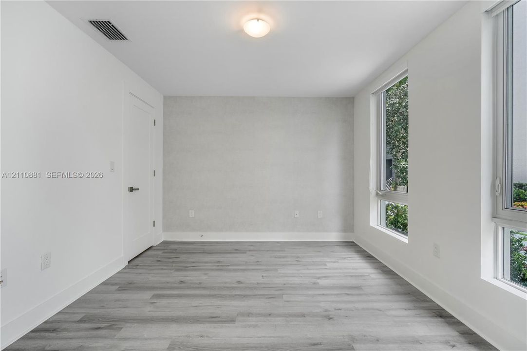 Room featuring wood-finish flooring, crisp white walls, a single-panel interior door, and tall casement windows