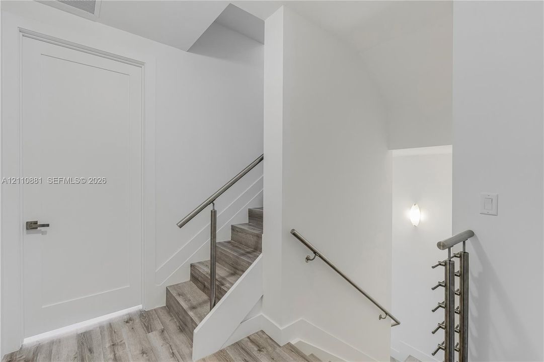 Staircase featuring wood-finish treads, stainless steel cable railing, and a wall-mounted metal handrail