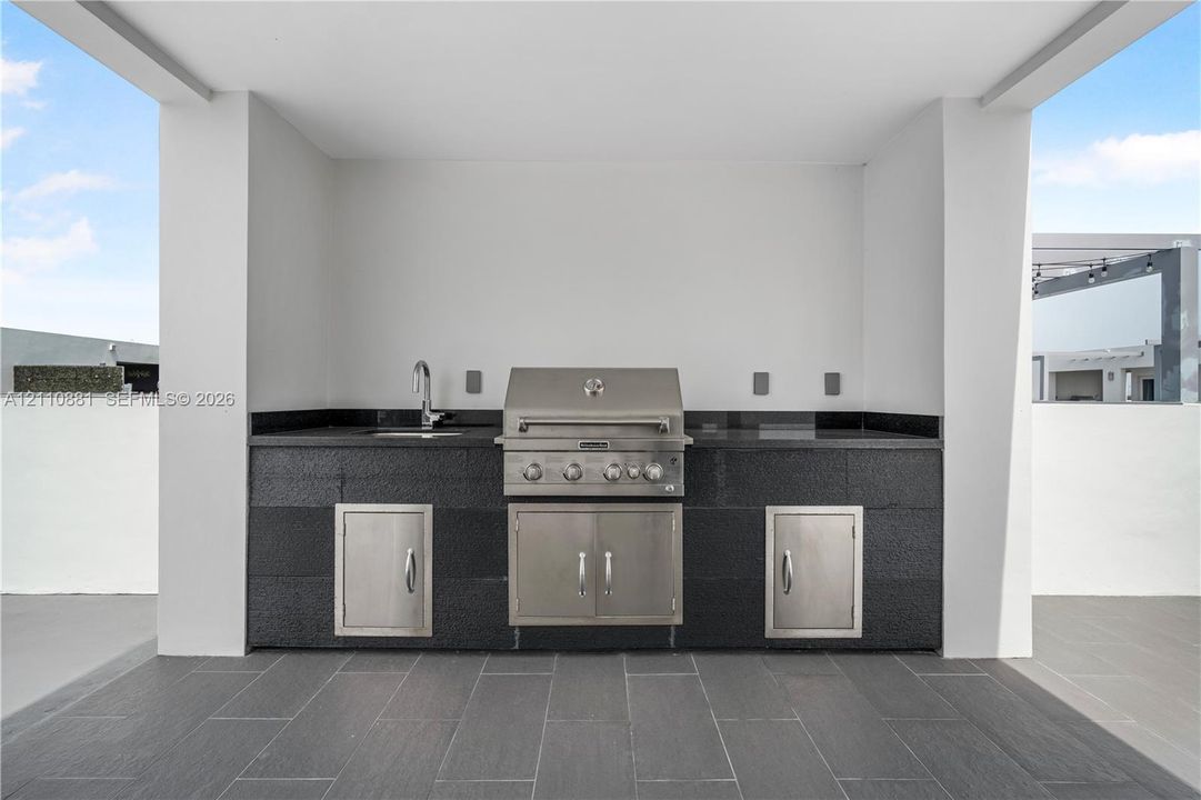 Covered outdoor kitchen featuring a built-in stainless steel grill, dark stone countertop, undermount sink, and stainless steel cabinetry