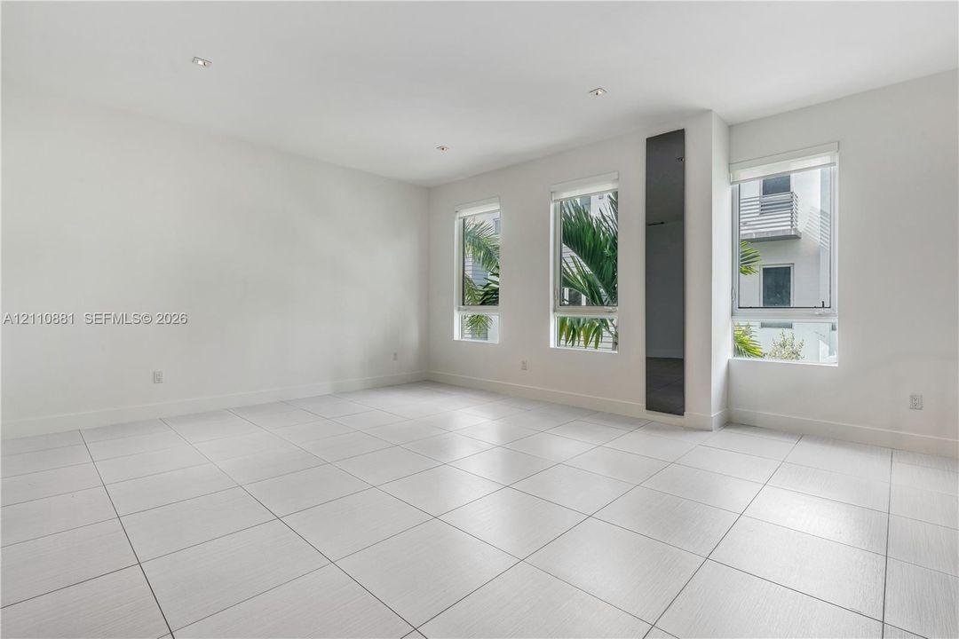 Open interior space featuring light-toned tile flooring, recessed ceiling lighting, three windows with roller shades, and a vertical charcoal-colored accent panel