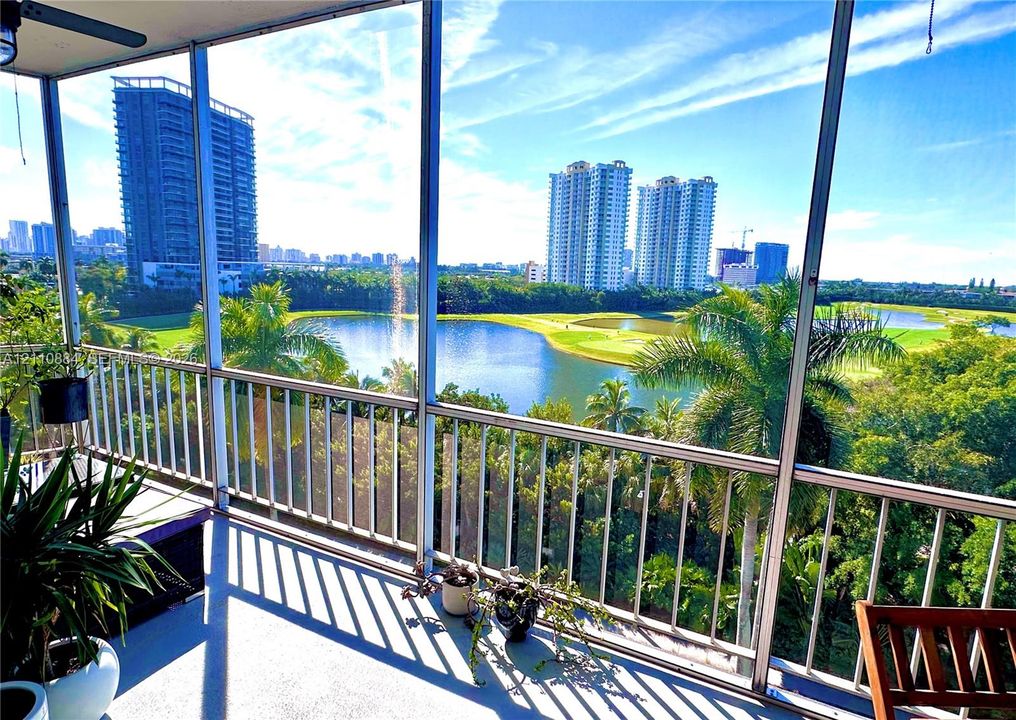Screened balcony featuring metal railings, overhead ceiling fan, and concrete flooring, overlooking a lake, golf course, and tropical oasis  landscape