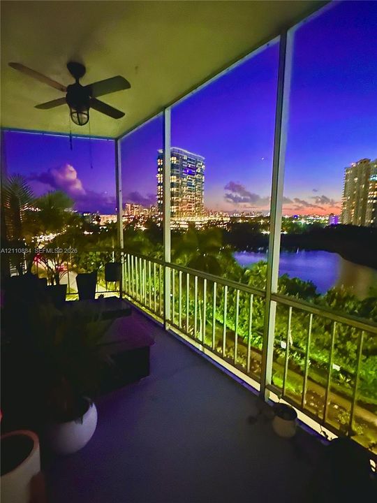 Screened-in balcony featuring a ceiling-mounted fan and metal railing, overlooking water and urban skyline