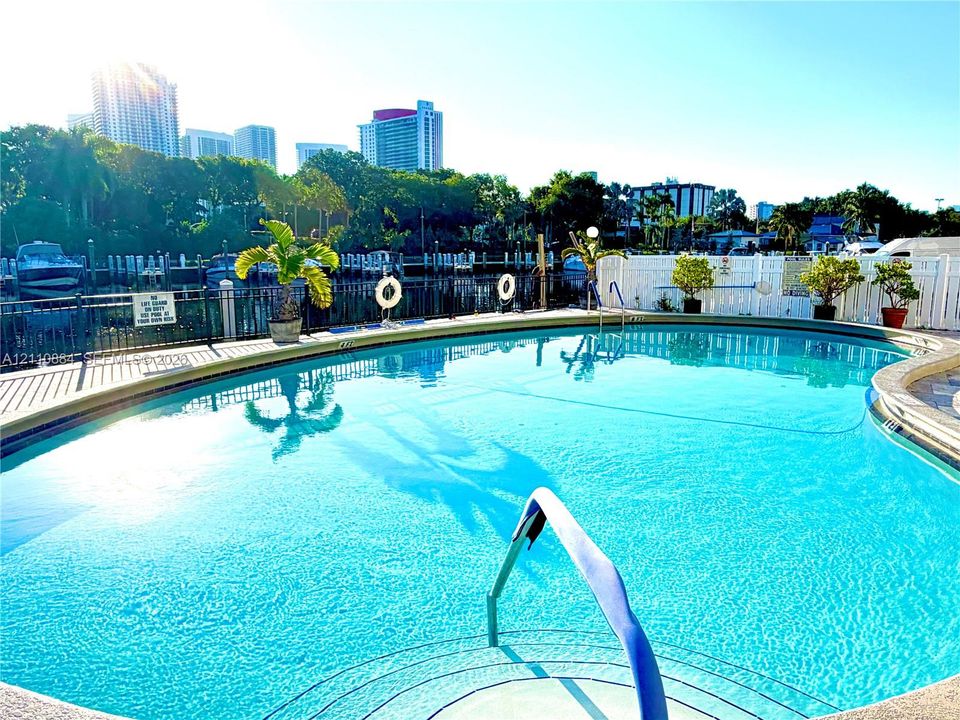 Curved swimming pool featuring a built-in step entry, metal perimeter fencing, and concrete decking