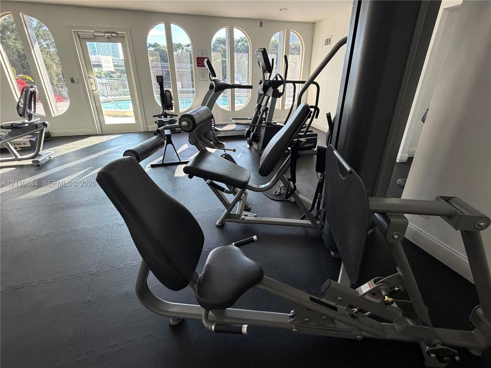 Fitness center featuring arched windows, dark rubberized flooring, and glass-paneled entry door