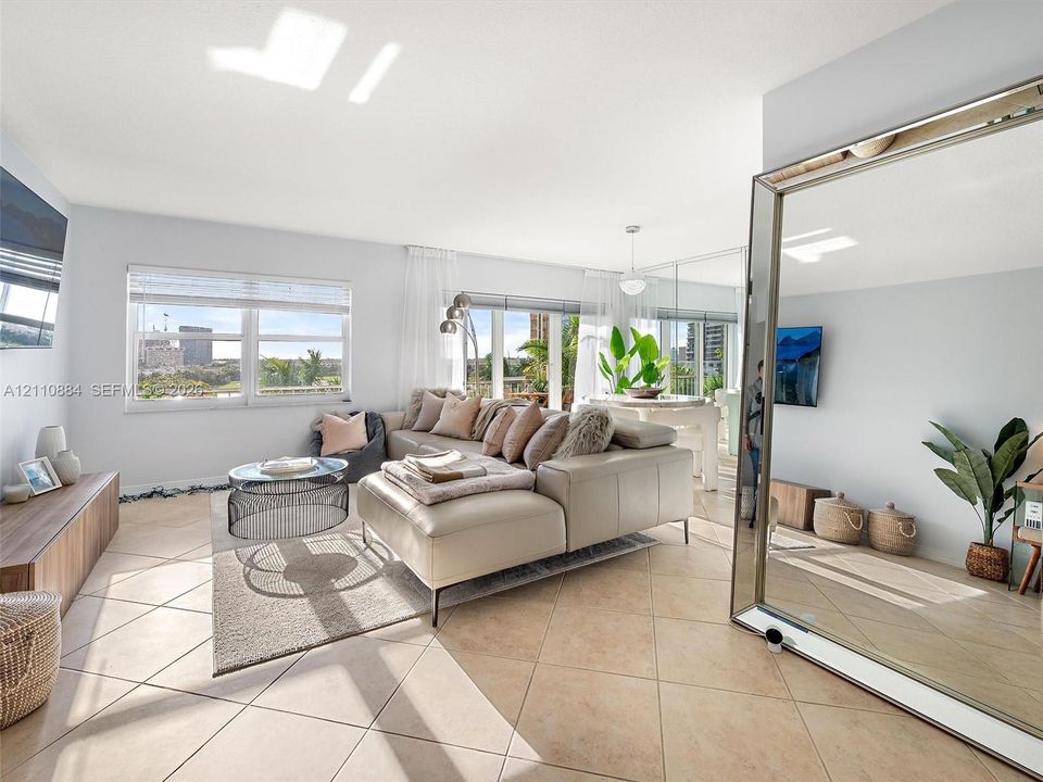 Open-concept living space featuring large-format ceramic tile flooring, expansive windows with exterior cityscape, and wall-to-wall mirror paneling