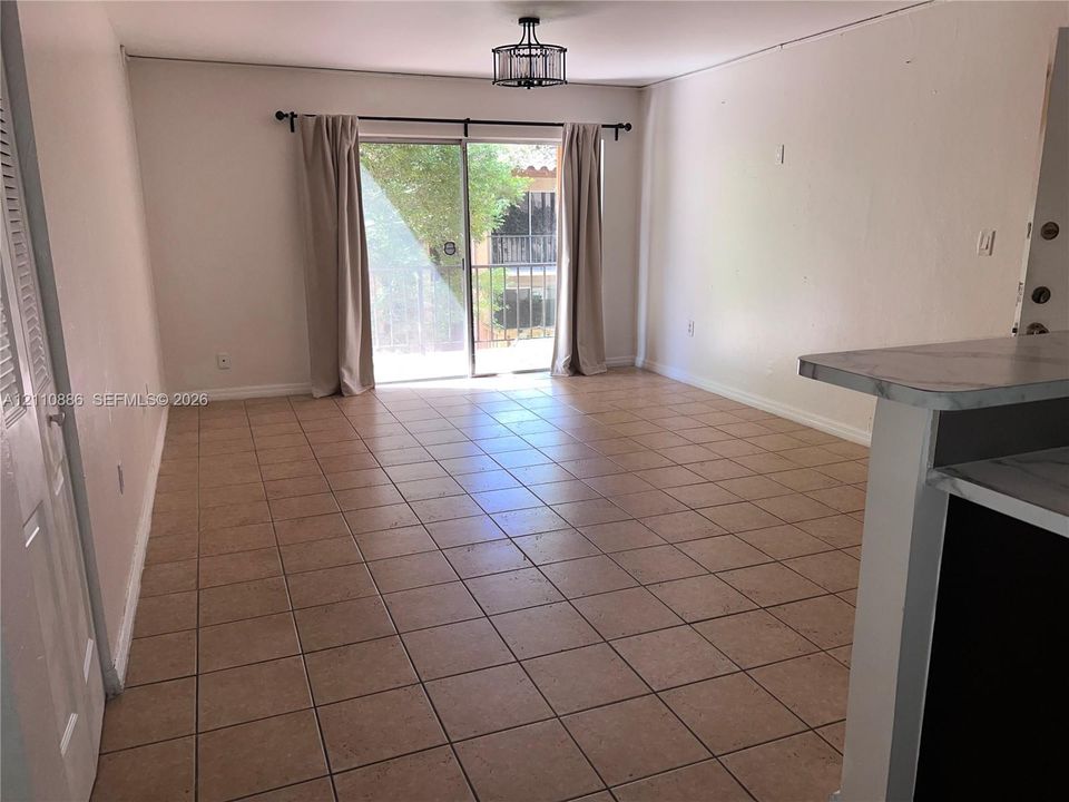 Ceramic tile flooring, sliding glass door with access to a balcony, drum-style ceiling light fixture, and a built-in counter with a stone-finish surface