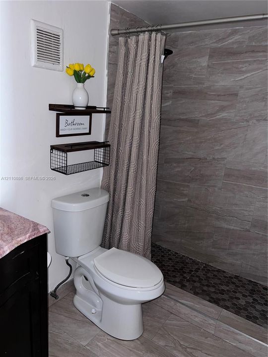 Shower area featuring large-format stone-look wall tiles and a dark, hexagonal tile floor, paired with a dark-toned vanity cabinet and stone countertop