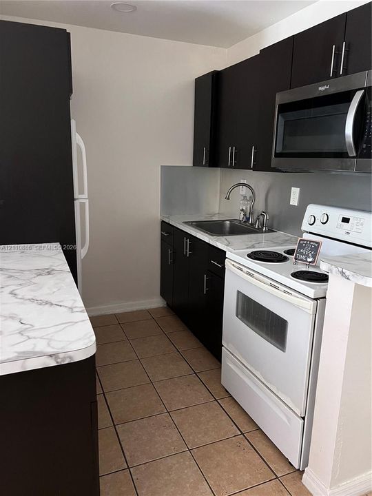 Kitchen featuring dark cabinetry, stone-patterned countertops, a stainless steel sink with a high-arch faucet, and recessed lighting
