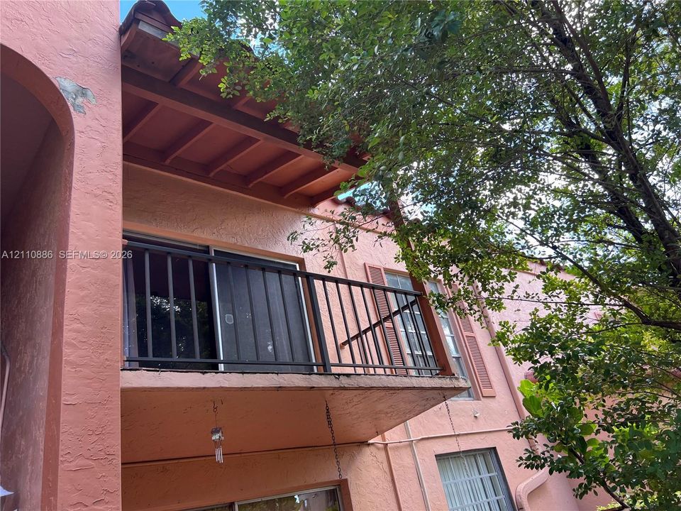 Stucco exterior featuring a second-story balcony with a metal railing, exposed beam ceiling, and shutter-framed windows