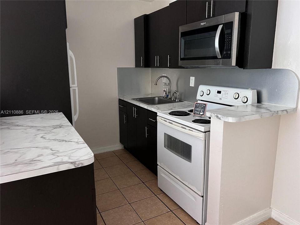 Kitchen featuring dark cabinetry, stone-finish laminate countertops, ceramic tile flooring, and integrated stainless steel appliances