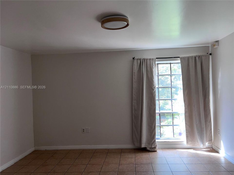 Neutral-toned walls, tile flooring, multi-pane window with wood-trim finish, and a circular flush-mount ceiling light