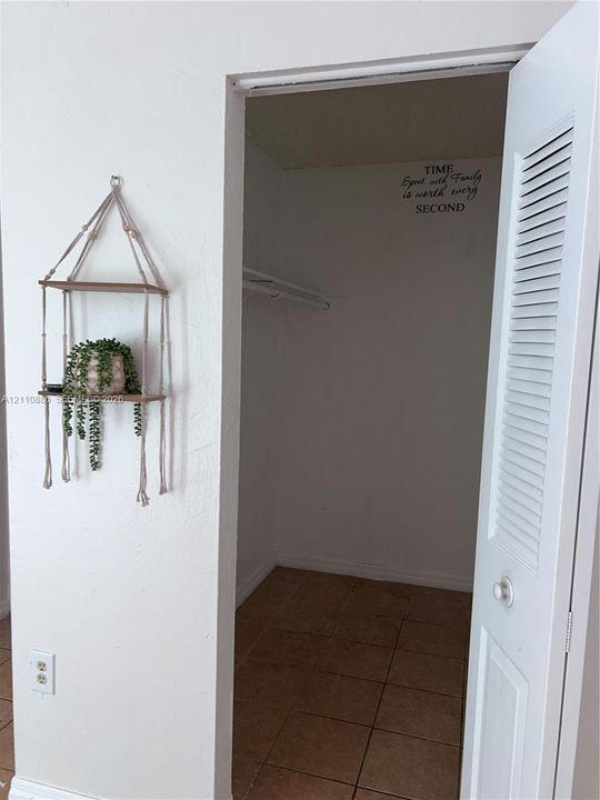 Reach-in closet featuring a white louvered door, interior wire shelving, and tile flooring