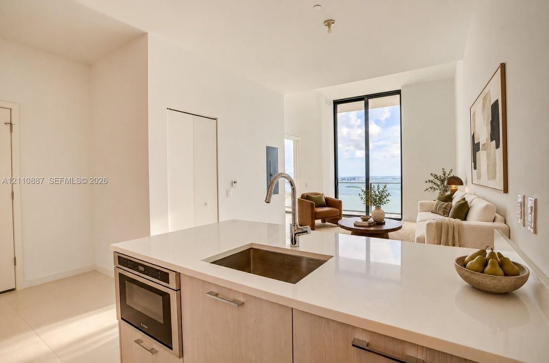 Kitchen featuring a stone countertop, stainless steel undermount sink, high-arc faucet, and built-in microwave, complemented by light-toned cabinetry and expansive floor-to-ceiling windows