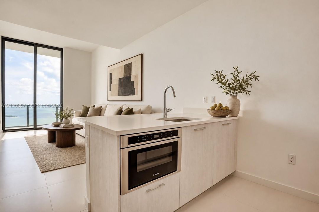 Kitchenette featuring light-finish cabinetry, quartz countertops, an integrated microwave, and a stainless steel undermount sink