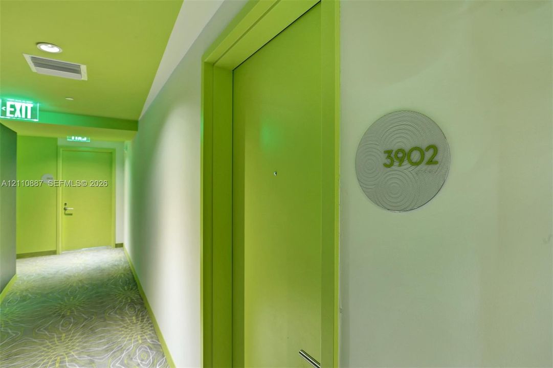 Hallway featuring lime-toned door frames, recessed ceiling lighting, patterned wall-to-wall carpeting, and circular suite identification signage