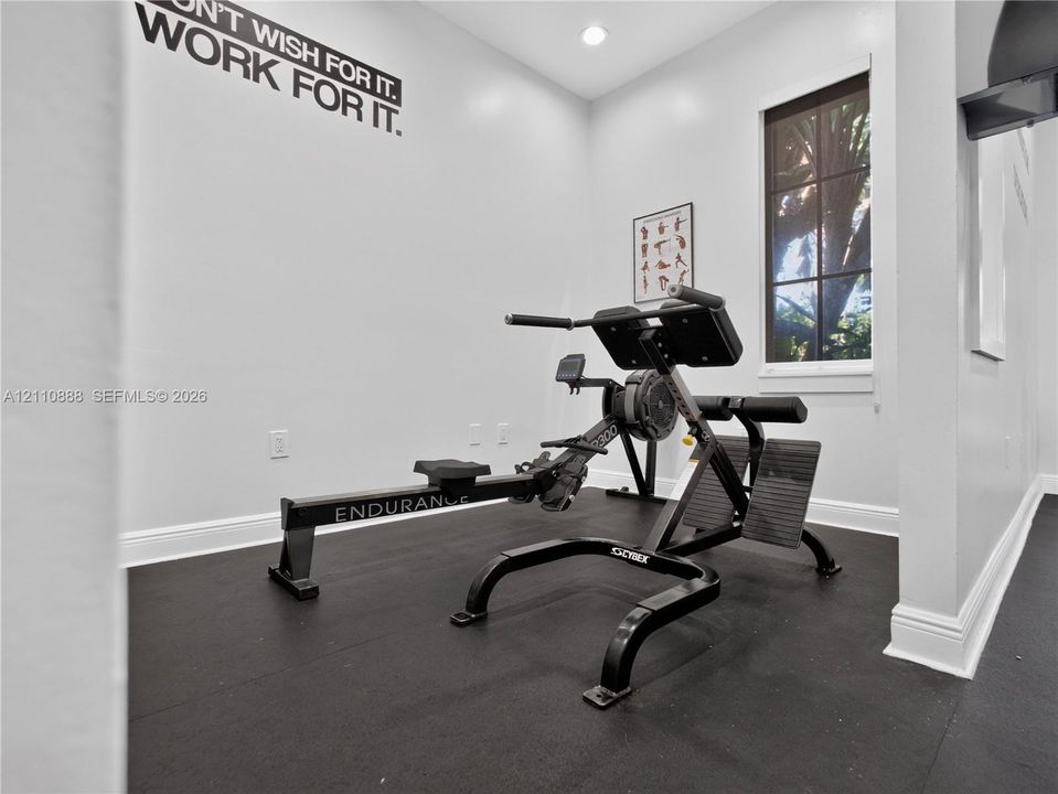 Interior room featuring dark rubberized flooring, crisp white walls, recessed ceiling lighting, and a window with a paneled frame