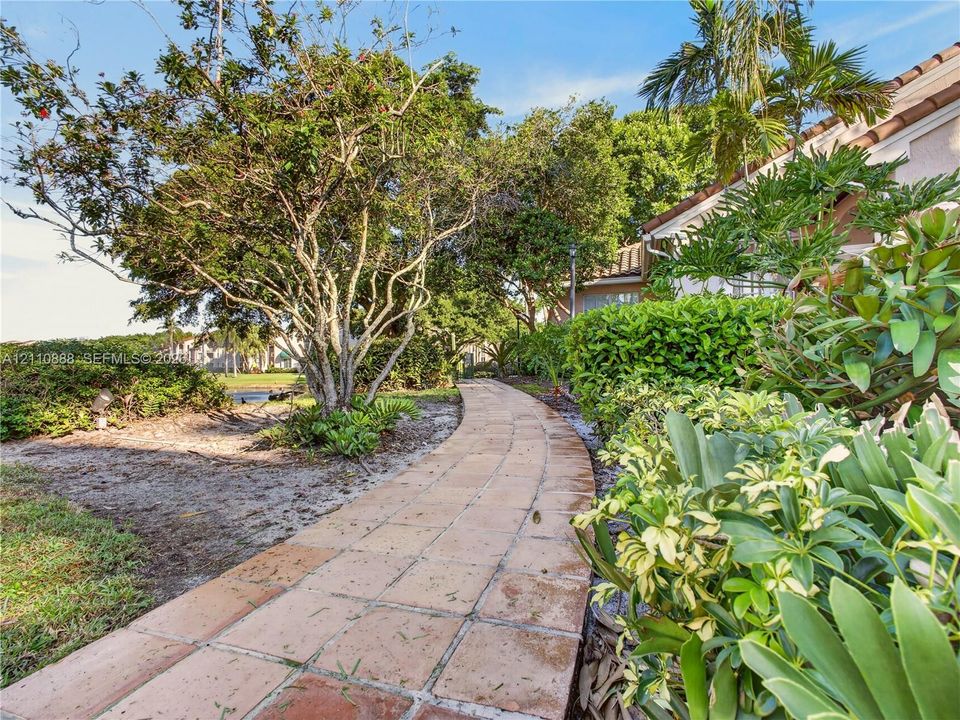 Paver walkway featuring mature trees, sculpted hedges, and tropical foliage
