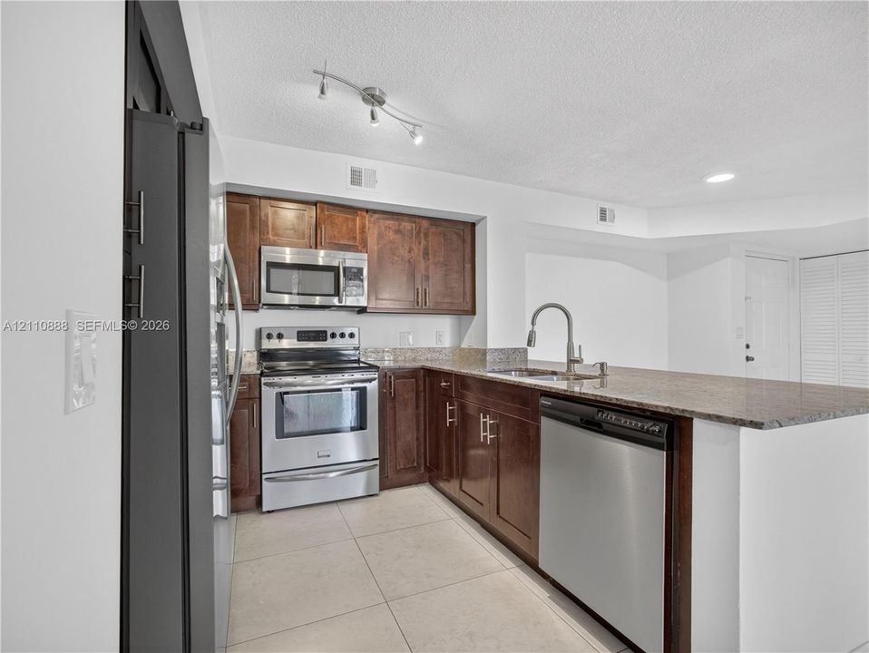 Kitchen featuring wood cabinetry, stone countertops, stainless steel appliances, tile flooring, and a multi-head track lighting fixture
