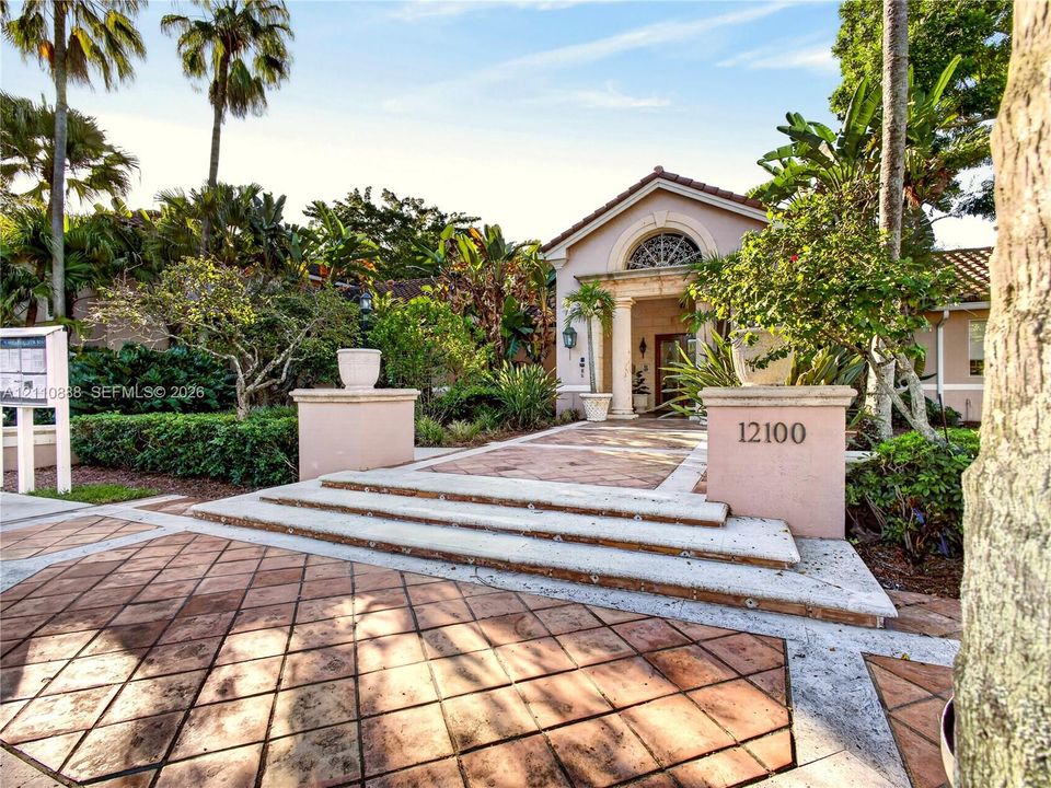 Stucco exterior featuring a covered entryway, arched transom window, columns, and a terracotta-tiled stone walkway with tiered concrete steps