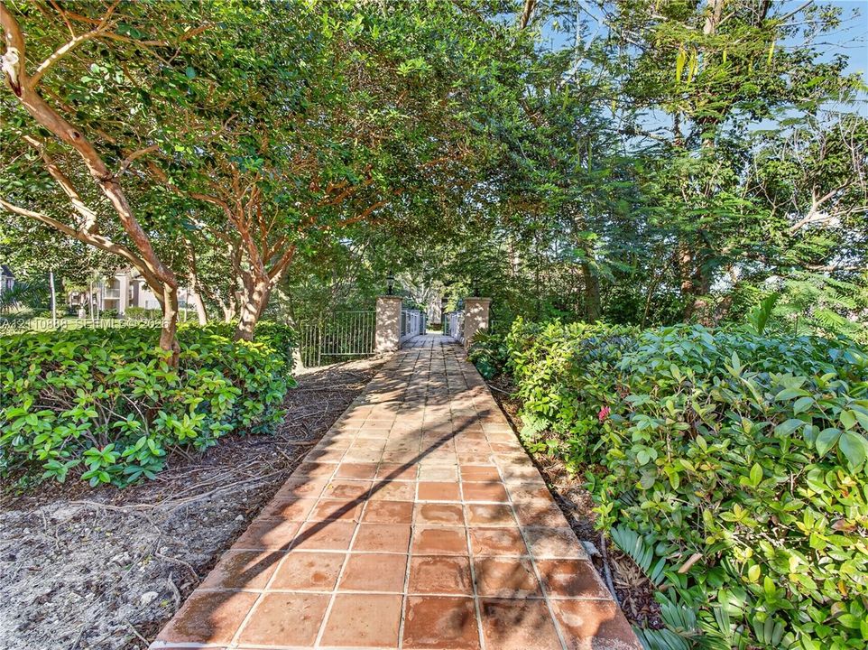 Terra cotta tile walkway framed by mature landscaping and metal fencing