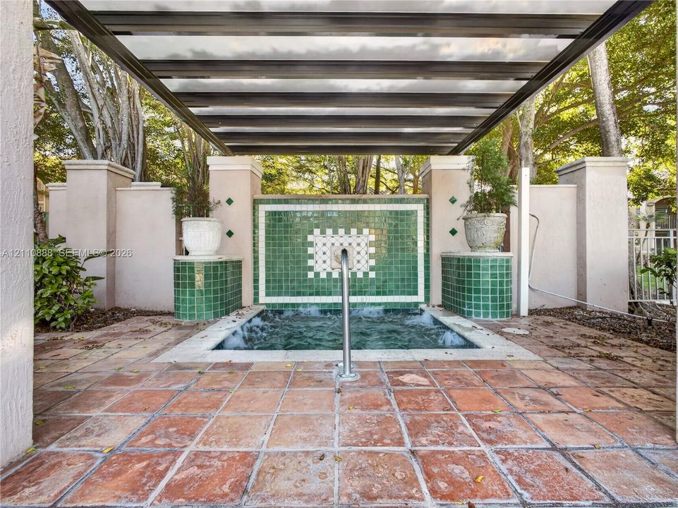 In-ground spa featuring a tiled water feature, overhead pergola, and terracotta-style flooring