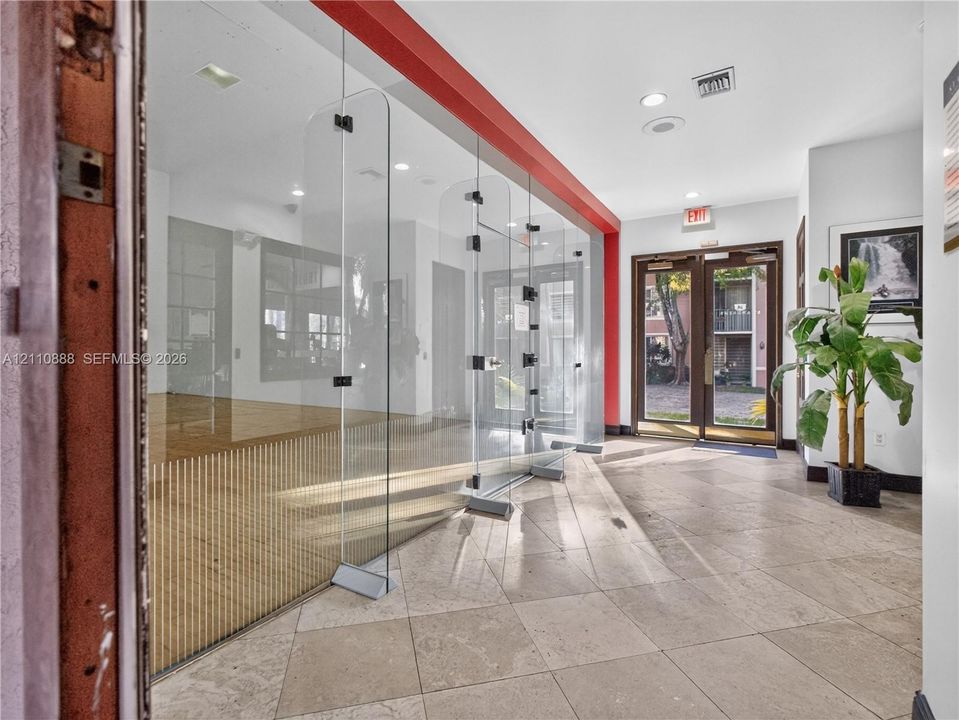 Interior lobby featuring large-format tile flooring, a floor-to-ceiling glass-paneled partition, recessed lighting, and double-door entryway