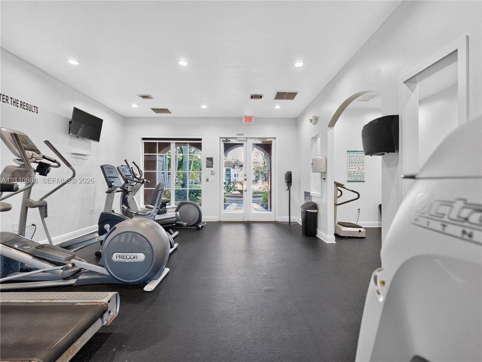 Fitness center featuring impact-resistant rubber flooring, recessed lighting, double glass-pane entry doors, and an arched architectural opening