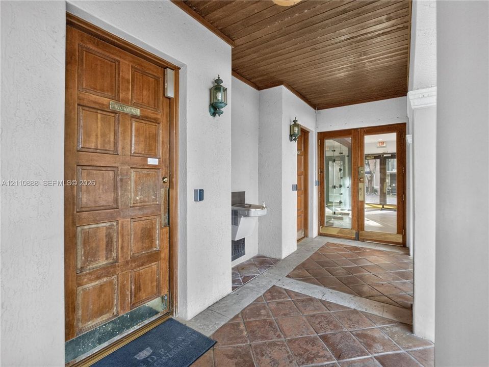 Covered entryway featuring a natural wood-finish plank ceiling, recessed lighting, multi-panel wooden doors, and stone tile flooring