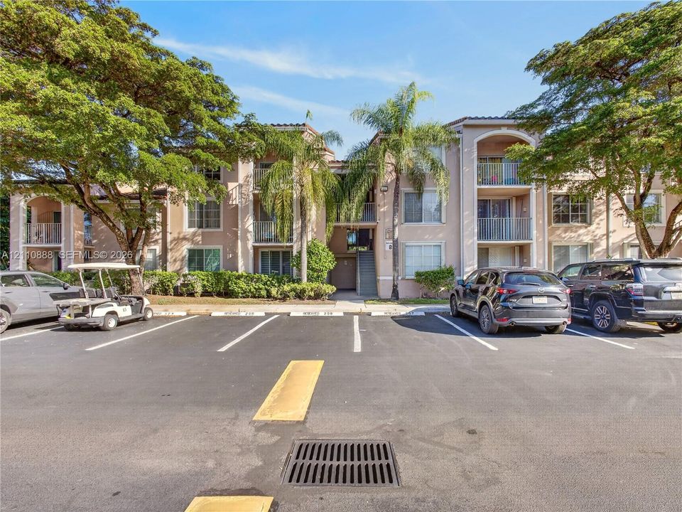 Stucco exterior featuring multiple private balconies with metal railings, mature landscaping, and dedicated parking
