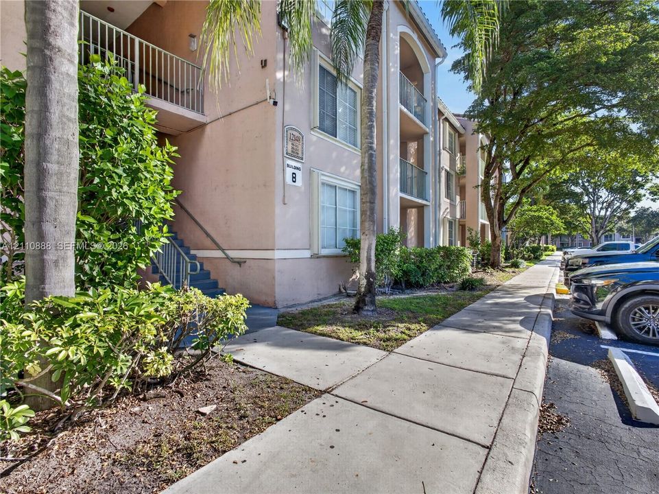 Multi-story exterior featuring a painted stucco facade, private balconies with metal railings, and concrete sidewalk access