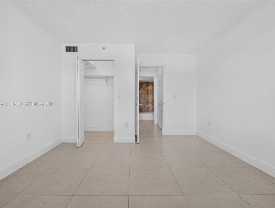 Neutral-toned tile flooring, white walls, and a walk-in closet with built-in shelving