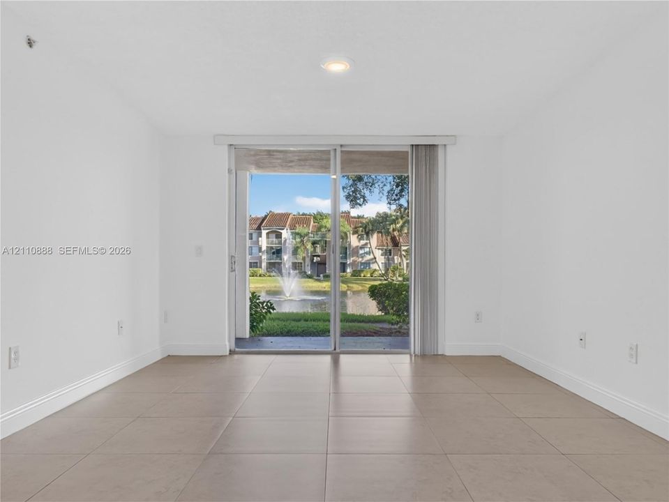 Interior room featuring neutral large-format tile flooring, recessed lighting, and a sliding glass door opening to a covered patio with water and fountain scenery