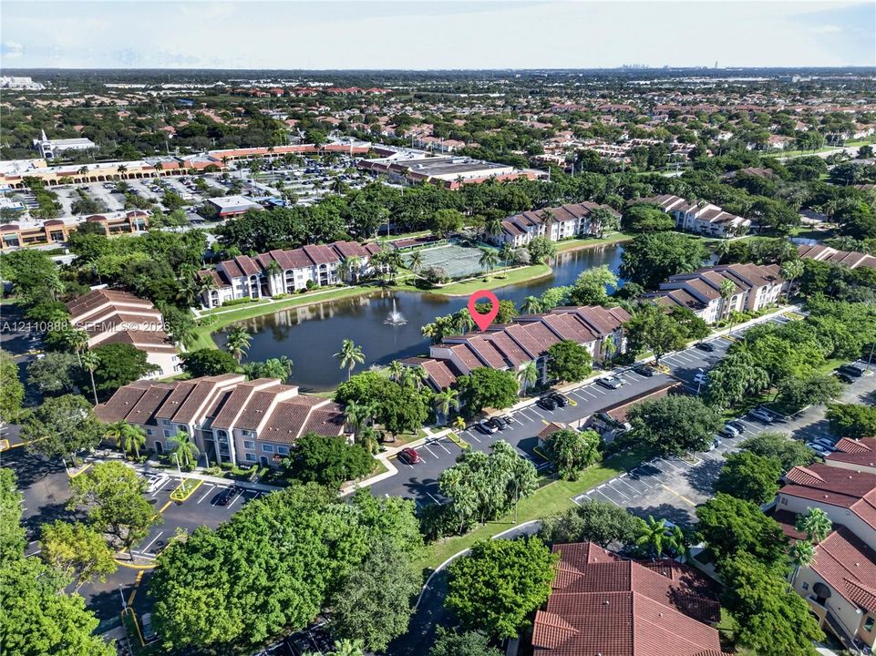 Multi-unit residential complex featuring tile roofing, surface parking areas, and mature landscaping surrounding a central water feature with a fountain
