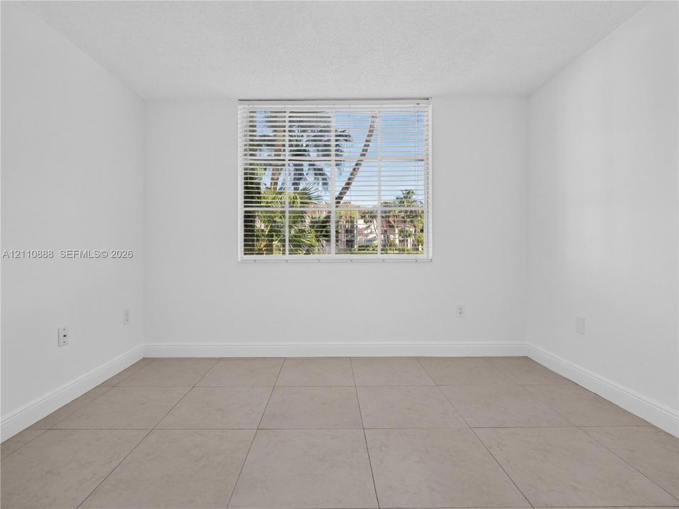 Neutral-toned ceramic tile flooring, clean white walls, and a large window with horizontal blinds