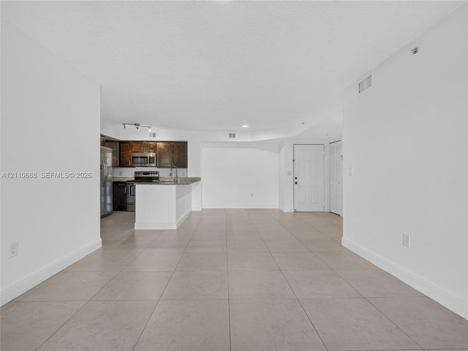 Open floor plan featuring large-format ceramic tile flooring, kitchen with dark cabinetry, stone-surface countertops, stainless steel appliances, and louvered closet doors