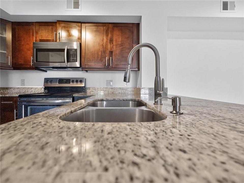 Kitchen featuring stone countertops, stainless steel undermount double-basin sink, high-arc pull-down faucet, stainless steel appliances, and dark-finish wood cabinetry