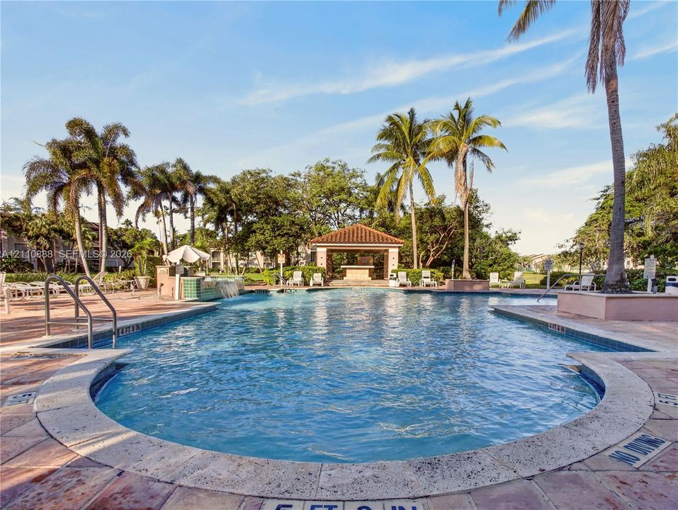 Swimming pool with stone-tiled decking, integrated water feature, and a covered pavilion