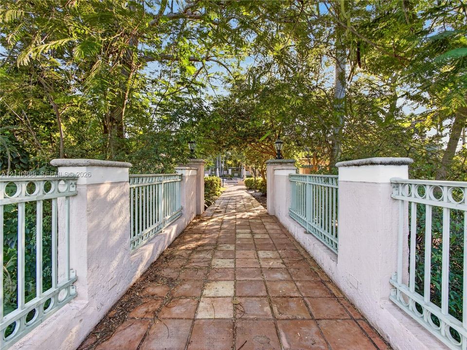 Pedestrian bridge featuring a tile-paved walkway, stucco-finished masonry pillars, and decorative metal railings with integrated light fixtures