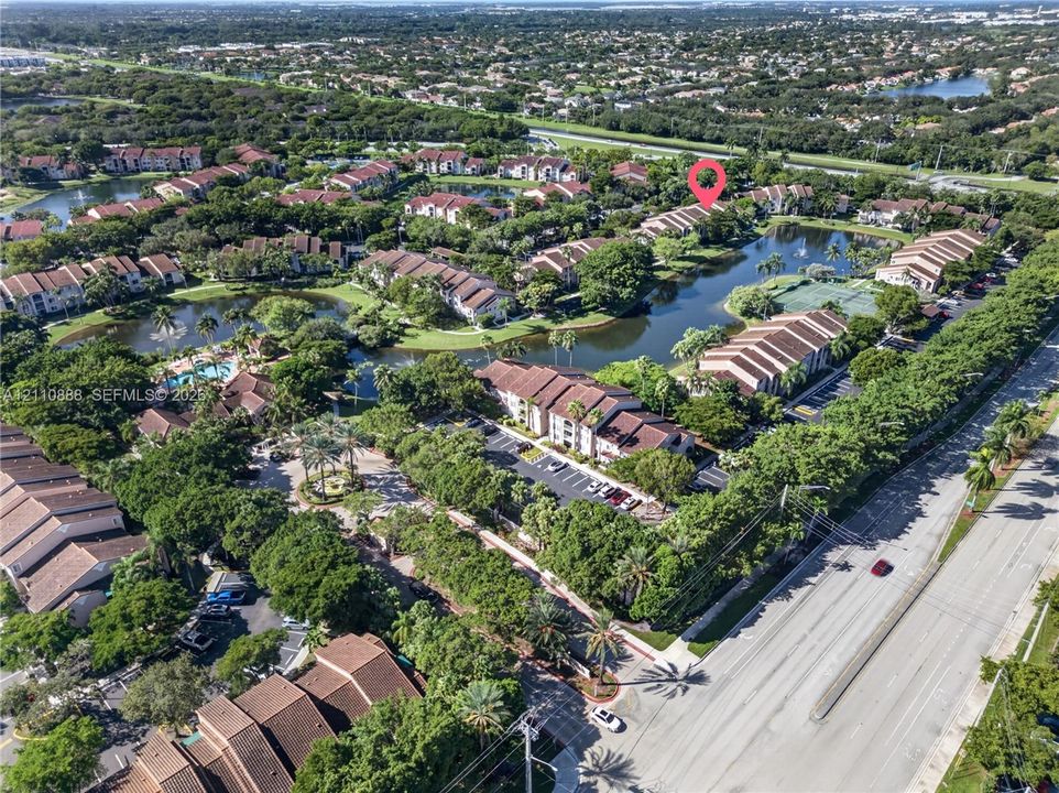 Aerial perspective of a multi-unit residential community featuring tiered rooflines, extensive water features, mature tree canopy, and paved parking areas