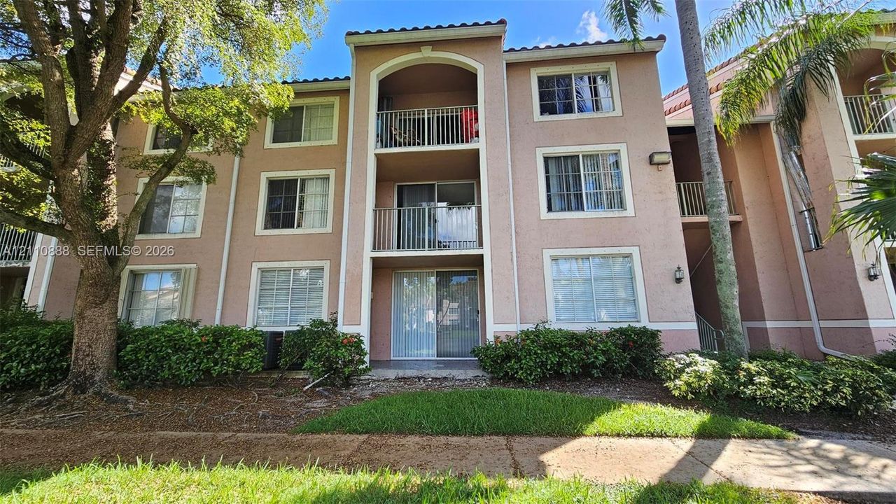 Multi-story stucco exterior featuring stacked private balconies, sliding glass door access, tiled roof accents, and mature landscaping