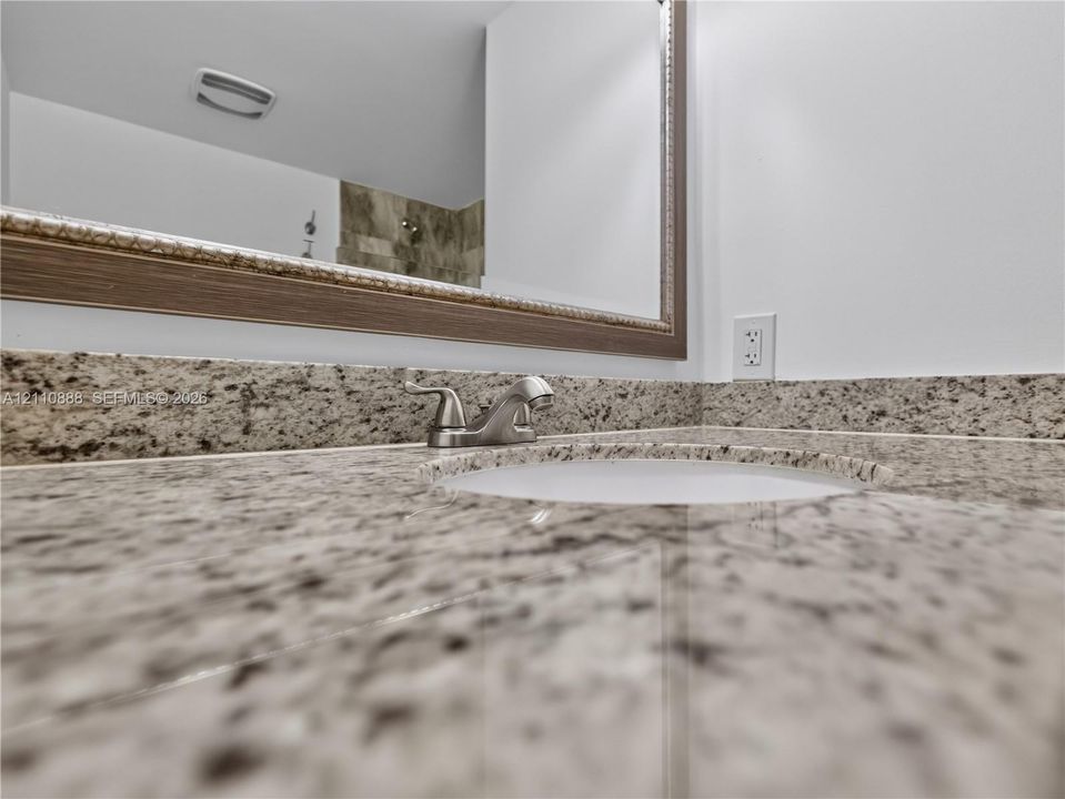 Stone countertop with integrated backsplash, under-mount sink, dual-handle faucet, and framed mirror