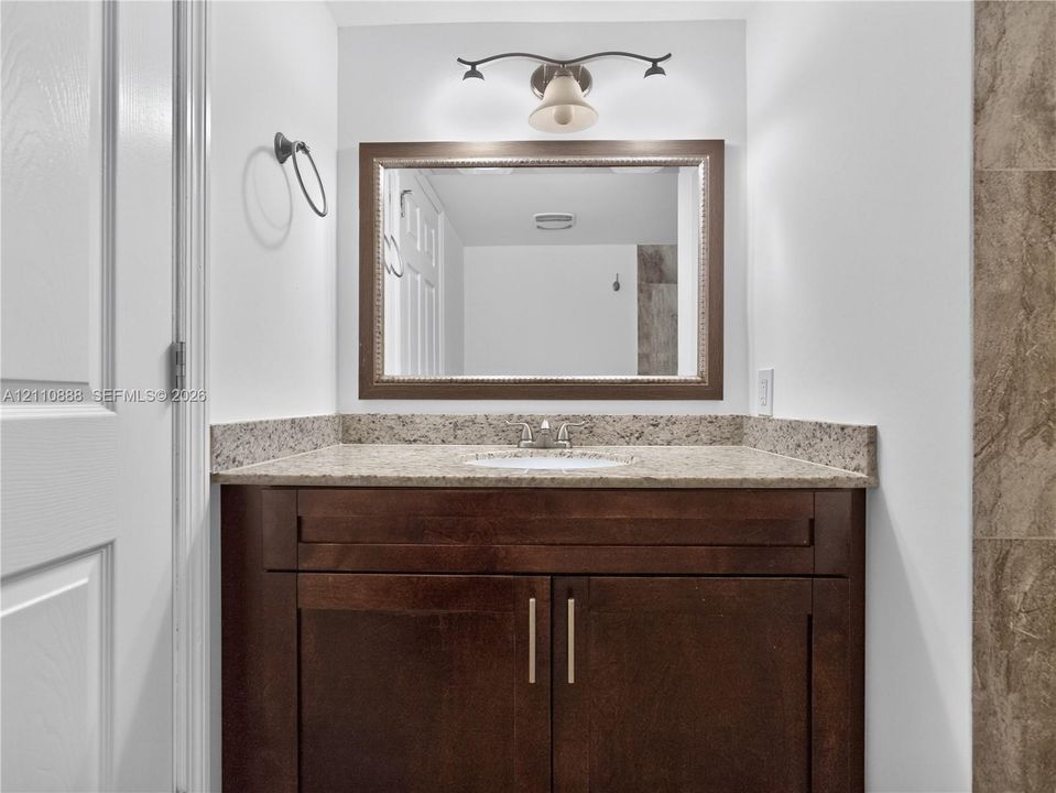 Dark wood cabinetry vanity with stone-finish countertop, integrated sink, framed wall mirror, and dual-bulb vanity lighting