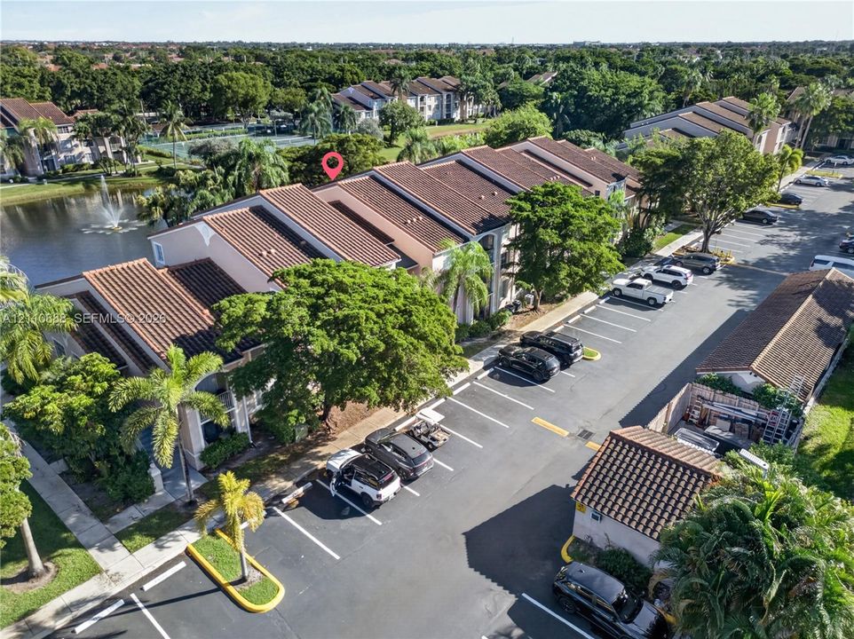 Multi-story residential structure featuring a terracotta-style tiled roof, stucco exterior, assigned parking area, and pond frontage