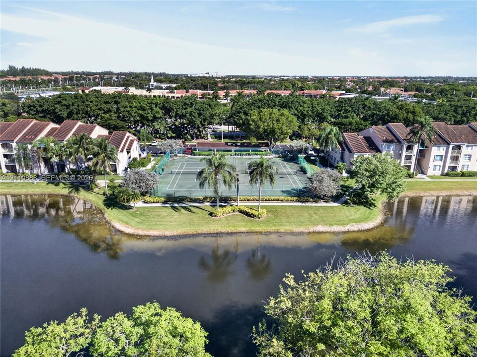 Tennis courts positioned within the community grounds, featuring a manicured lawn, perimeter fencing, and water frontage