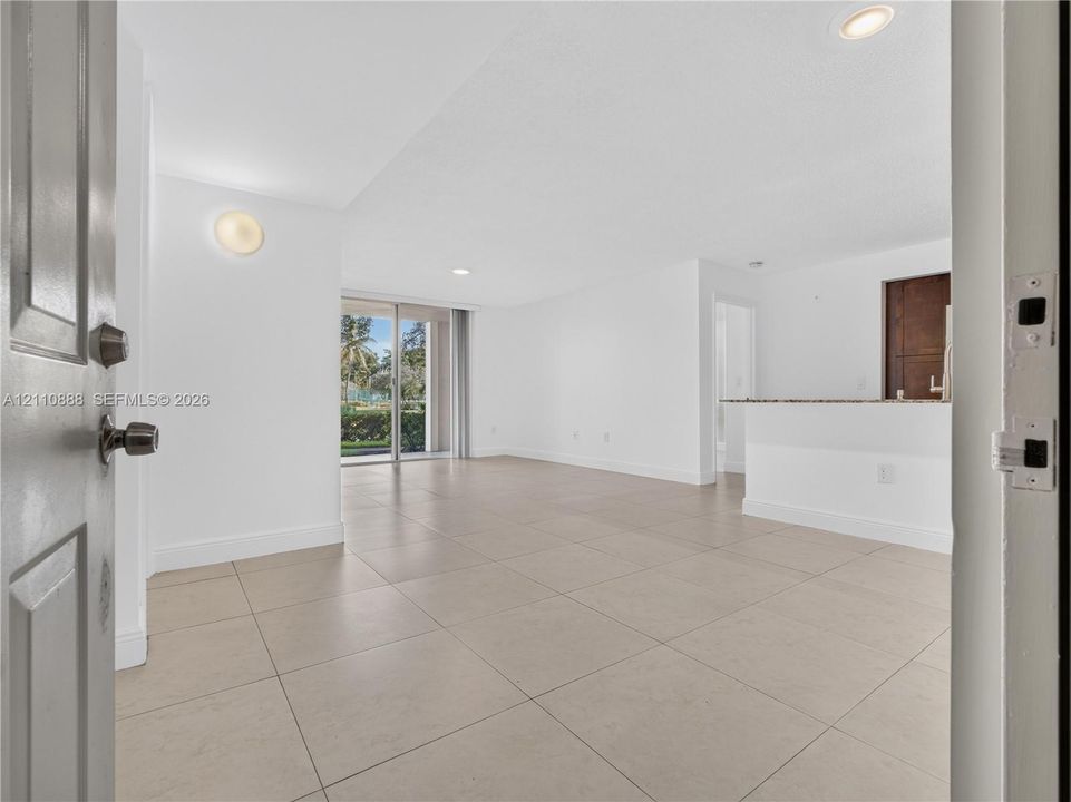 Open-concept interior featuring large-format tile flooring, recessed lighting, wall-mounted light fixtures, a stone-surfaced breakfast bar, and sliding glass doors