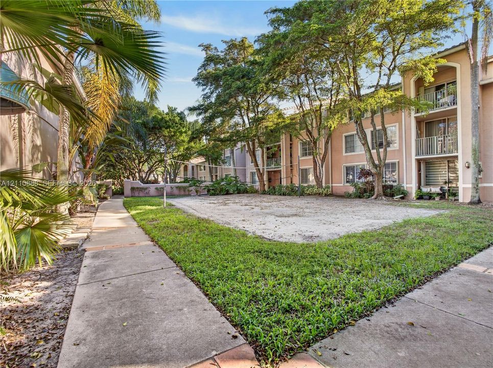 Sand volleyball court featuring a manicured lawn, concrete perimeter walkways, and mature landscape