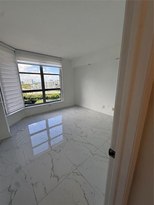 Room featuring large-format veined tile flooring and floor-to-ceiling windows with roller shades