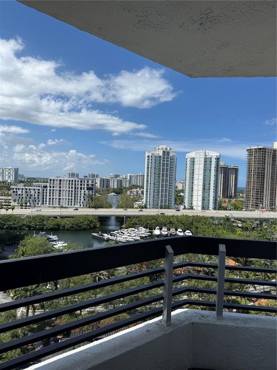 Private balcony featuring a black metal railing overlooking a waterway, boat slips, and an urban cityscape